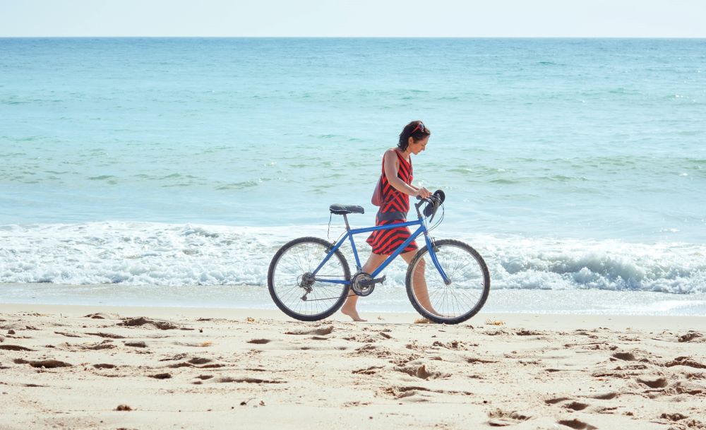 woman walking bike on the beach